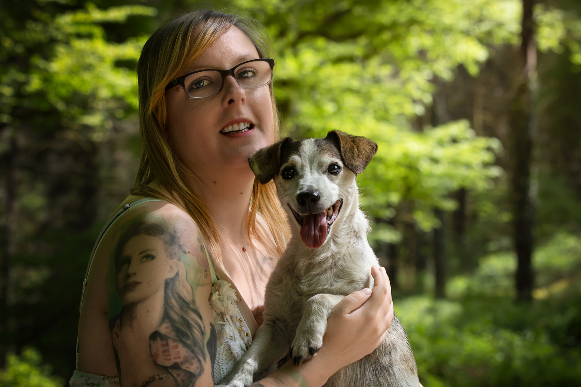 Coralie Jacques tenant un petit chien souriant dans ses bras en forêt