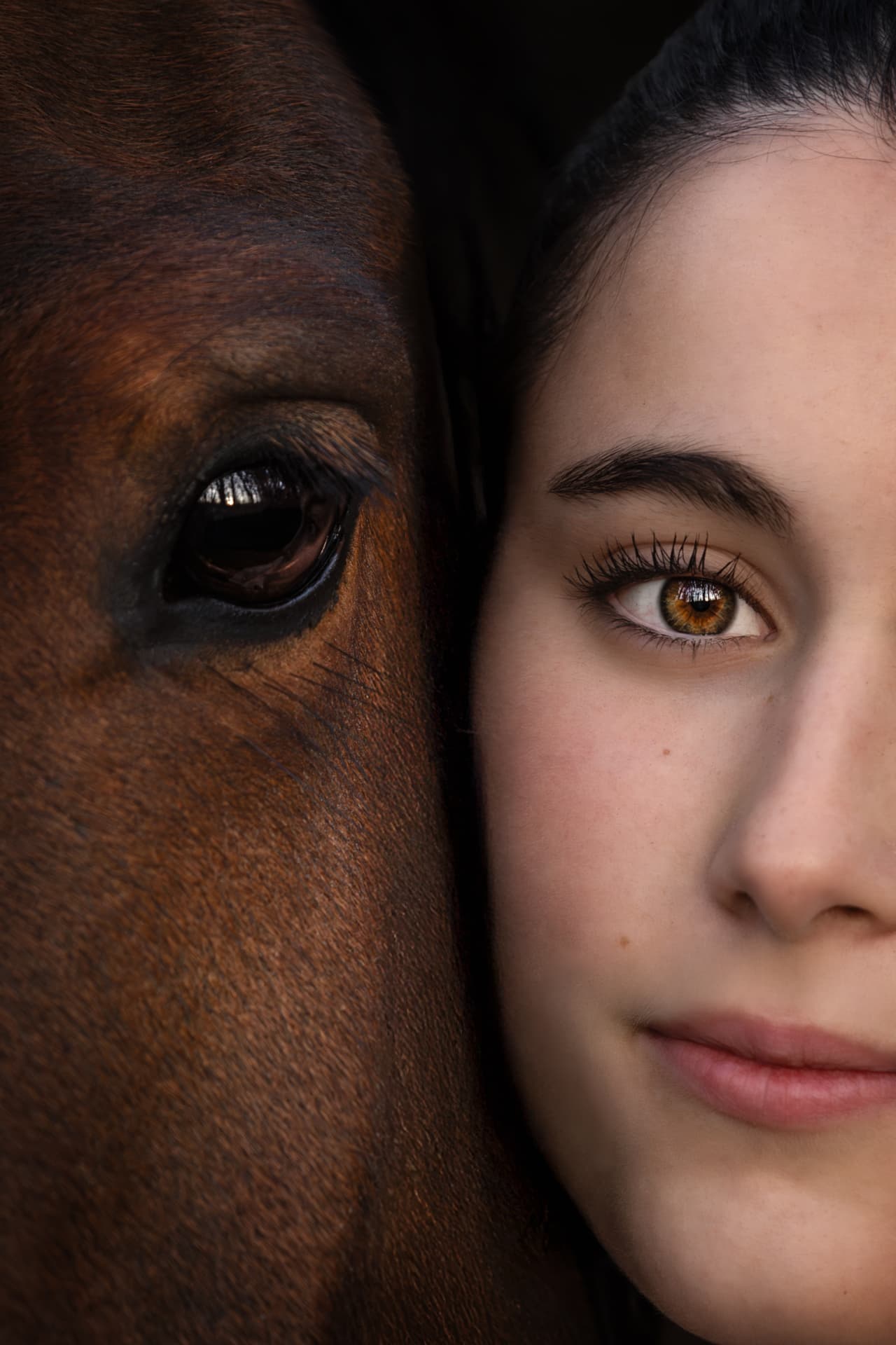 Visage d’une femme joue contre joue avec l’œil de son cheval, portrait en clair-obscur